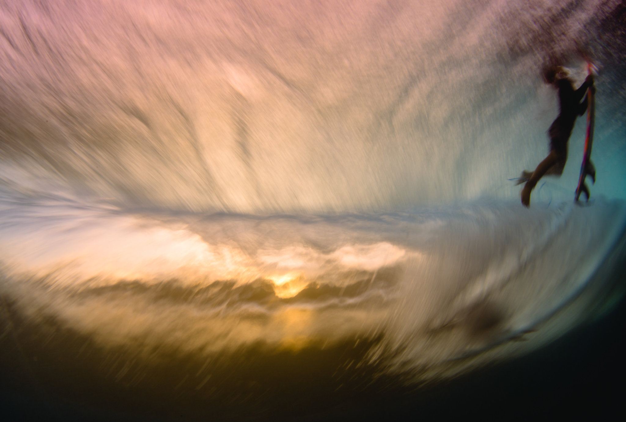 A surfer and board suspended beneath a wave in warm, refracted light