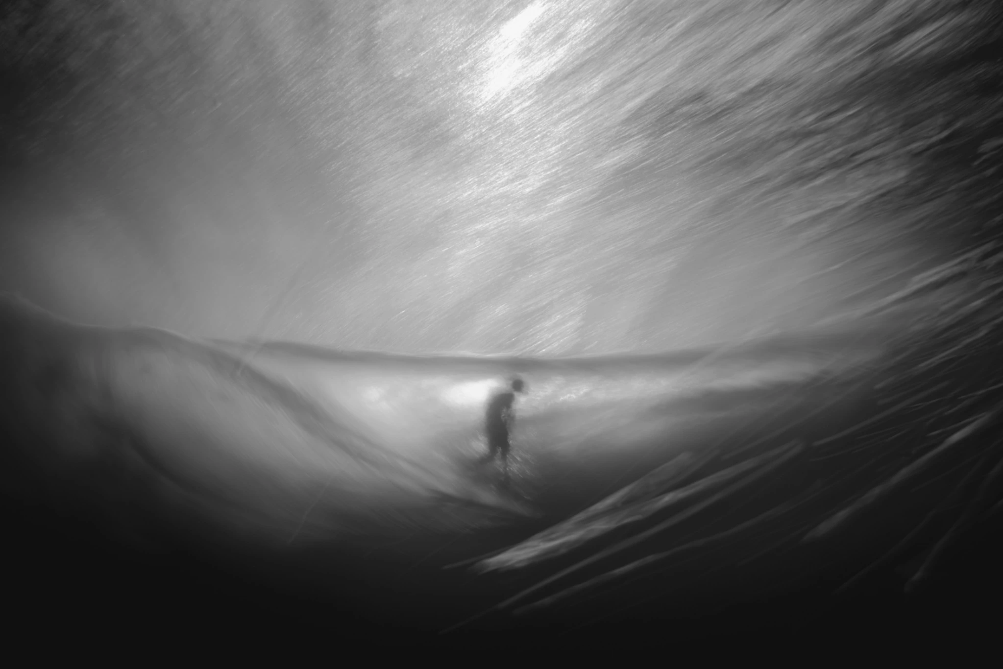 A surfer moving through a black-and-white, motion-blurred barrel; photograph mirrored horizontally